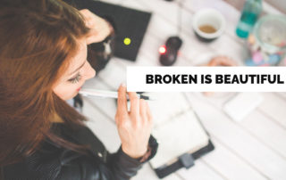 a woman at a desk working in a notebook labeled broken is beautiful
