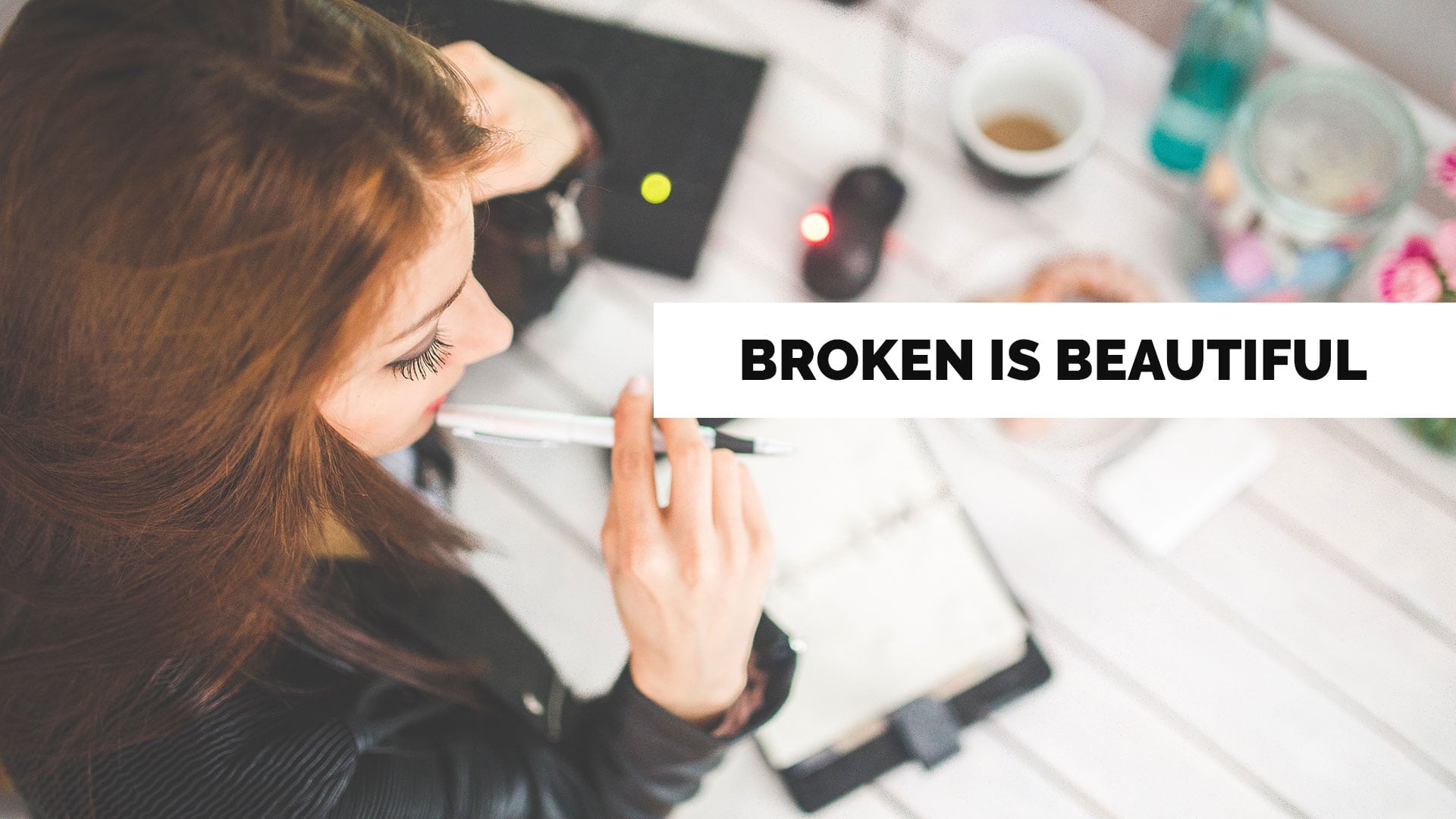 a woman at a desk working in a notebook labeled broken is beautiful