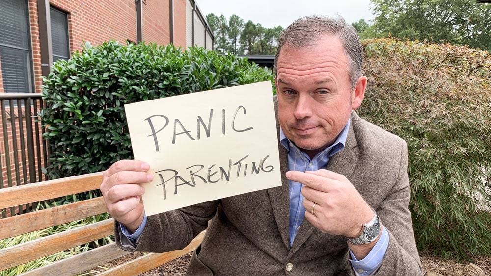 a man holding a sign that says panic parenting